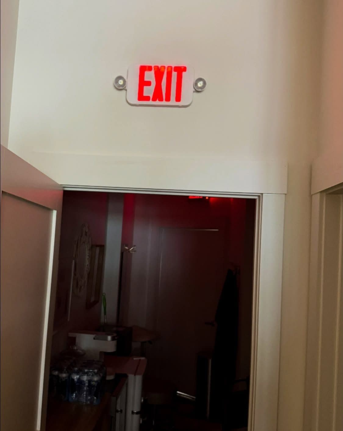 Illuminated exit sign with emergency lighting heads above a doorway